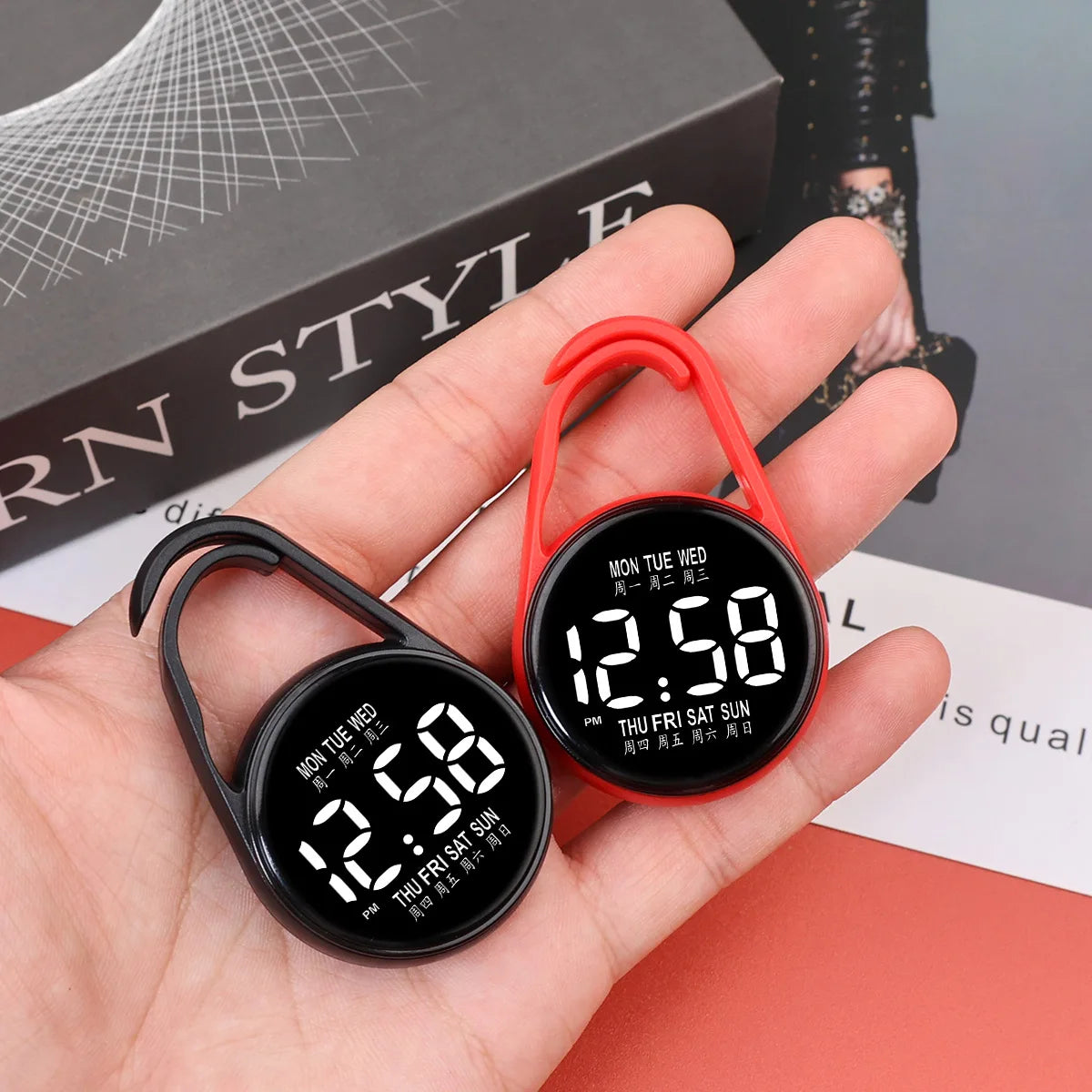A hand holds a digital LED hanging pocket watch with an orange strap and a black face displaying 12:58.