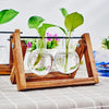 Una estación de propagación de madera sostiene dos frascos de vidrio con agua y esquejes de planta verde sobre un mantel blan
