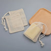 A set of natural cotton mesh soap saver pouches and a wooden soap dish on a gray background.