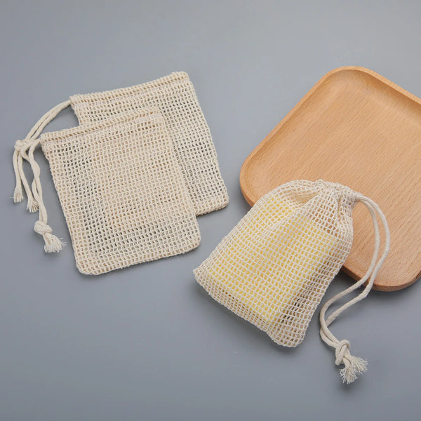 A set of natural cotton mesh soap saver pouches and a wooden soap dish on a gray background.
