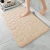 A beige 3D non-slip bathroom doormat with a textured surface is placed on a gray floor.