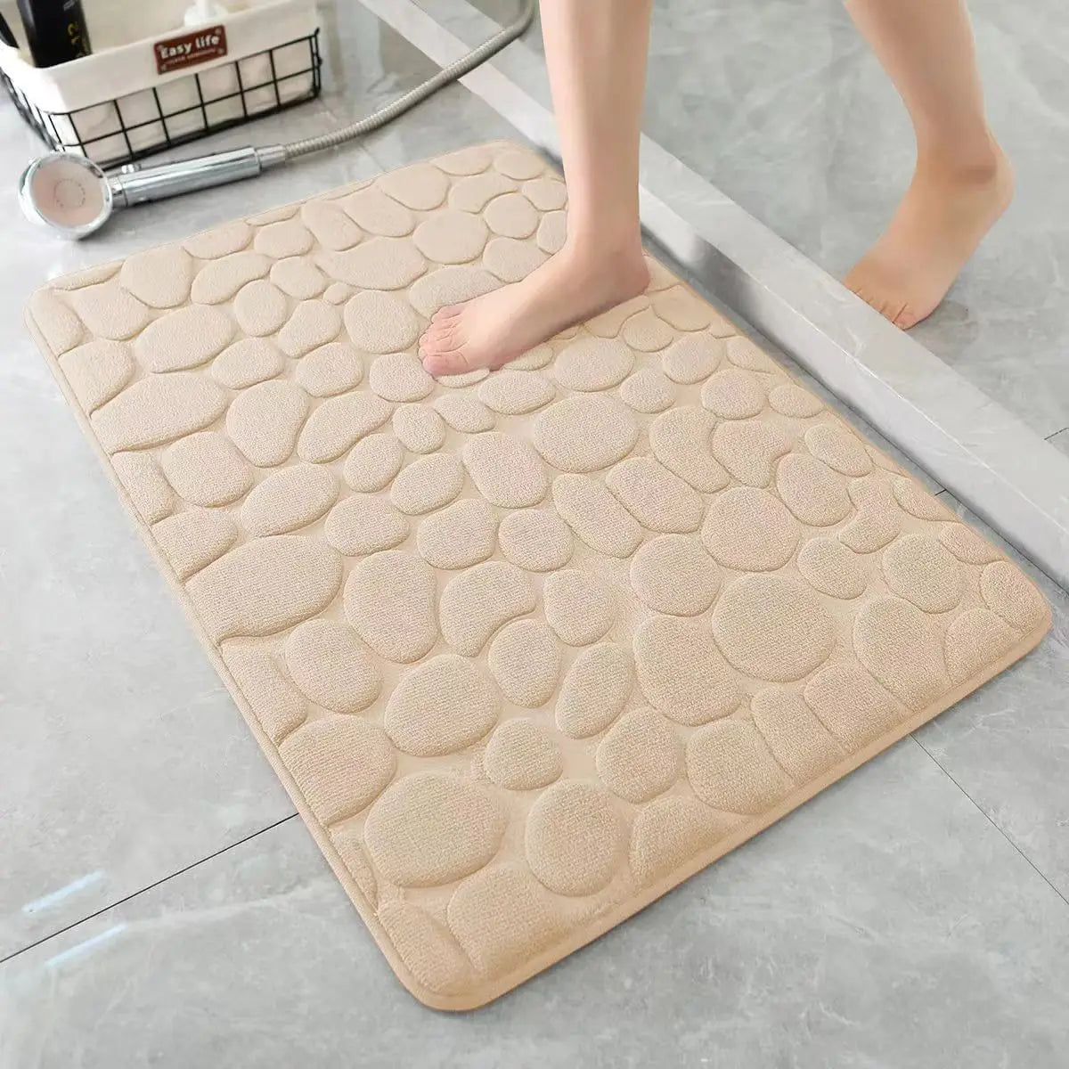 A beige 3D non-slip bathroom doormat with a textured surface is placed on a gray floor.