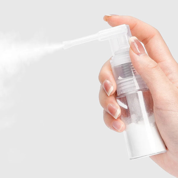 A hand sprays a white mist from a clear plastic bottle with a pump dispenser.