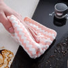 A hand holds a pink and white coral fleece cleaning cloth over a dark surface.