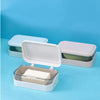 A white transparent drainage soap dish with a rectangular bar of soap is shown on a light blue background.