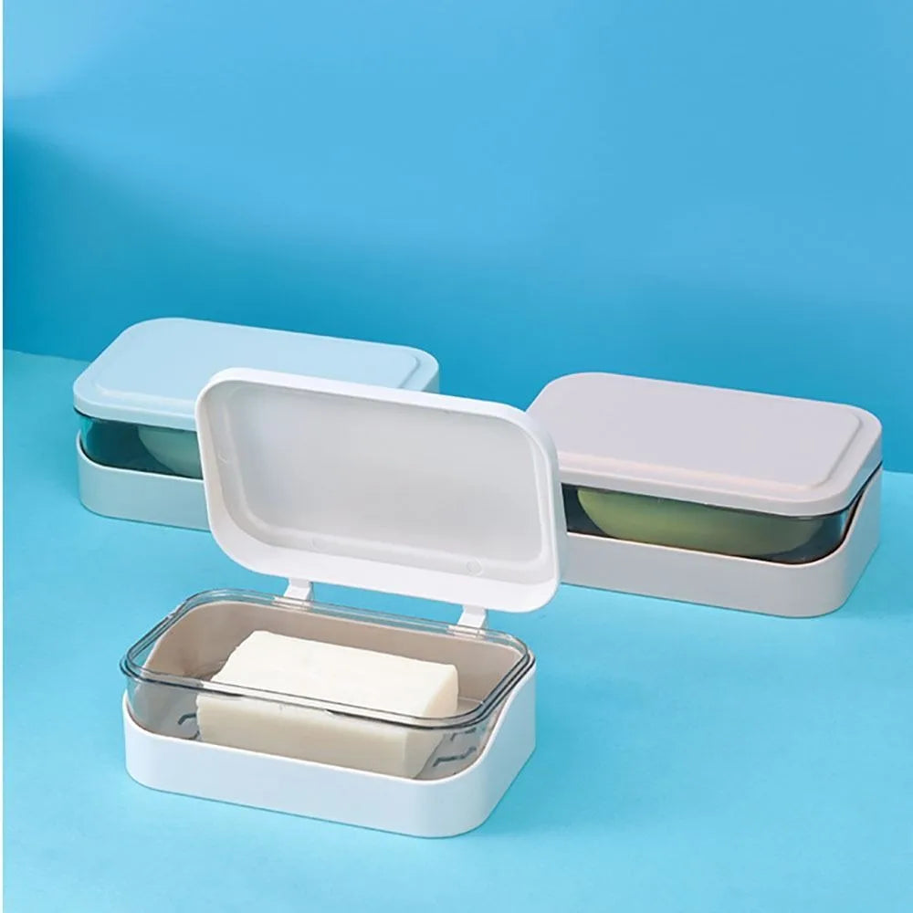A white transparent drainage soap dish with a rectangular bar of soap is shown on a light blue background.