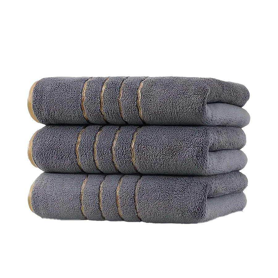 A stack of gray coral fleece towels with gold stripe detailing.