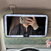 Espejo de maquillaje con luz LED montado en la ventana de un coche, mostrando a una persona usando un smartphone para tomar u