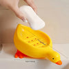 A yellow duck shaped soap dish with a self-draining tray and a white soap bar being placed on it.