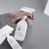 A hand is holding a white spray bottle with a pump dispenser, demonstrating the refillable plastic spray bottle for plants an