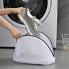 A hand is placing a gray shoe into a white mesh laundry bag for shoes, socks, and bras.
