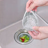 A hand is holding a reusable mesh strainer bag over a metal drain, showing the fine mesh texture.