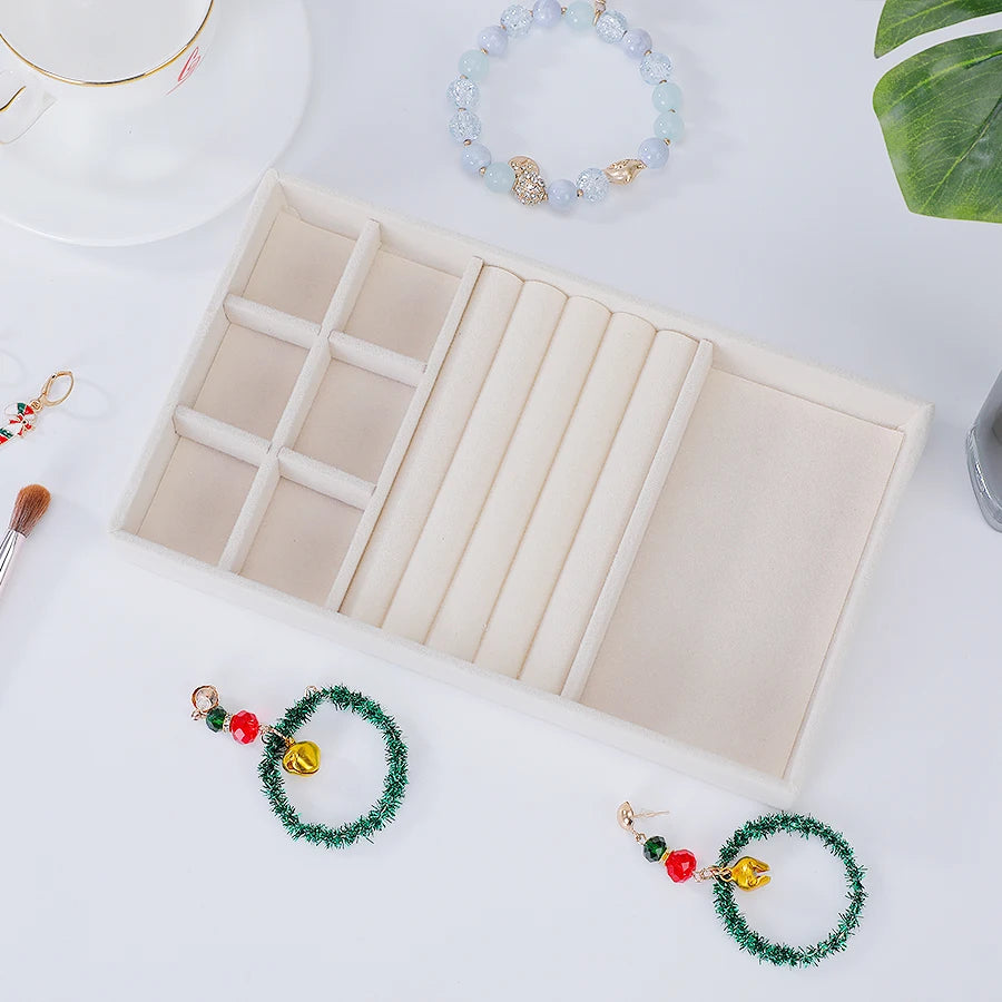 A light beige velvet jewelry organizer tray with a drawer and several beaded bracelets is displayed on a white surface.