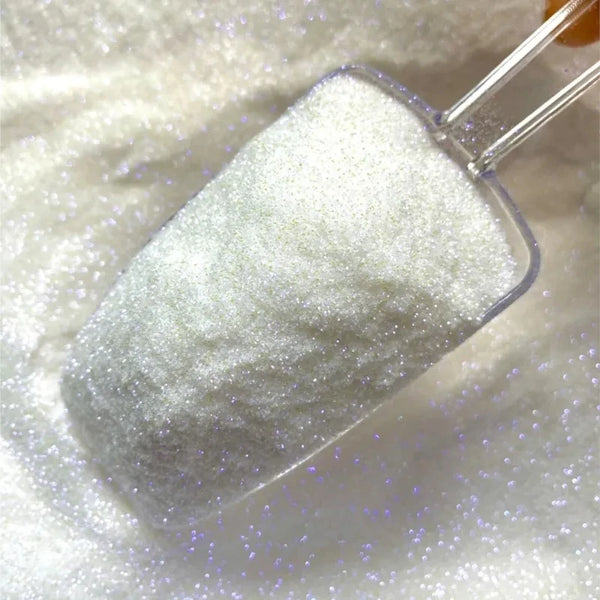 A small glass container filled with iridescent rainbow chrome nail glitter powder is shown on a white surface.