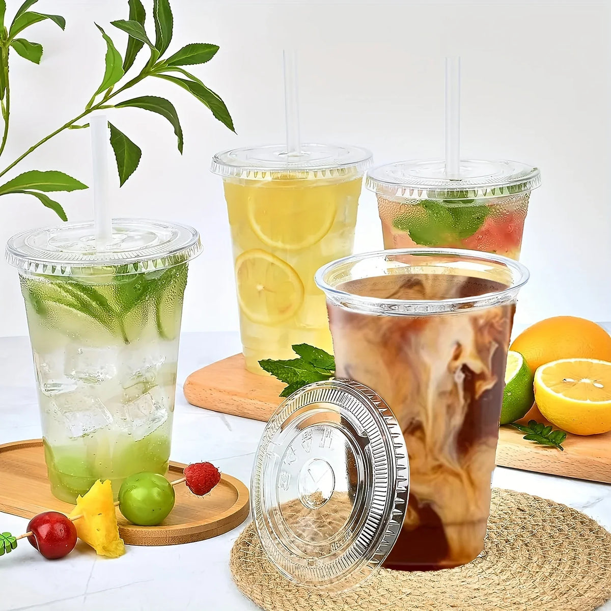 A glass of iced tea or juice in a clear plastic cup with a lid, surrounded by fresh fruit and a reusable plastic cup.