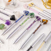 A collection of natural crystal pens featuring various colored stones like amethyst, quartz, and citrine on a white surface.