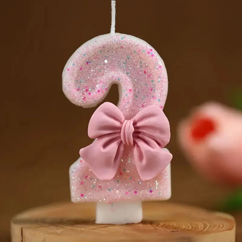 A pink glitter number 9 candle decorated with a pink bow on a wooden surface.