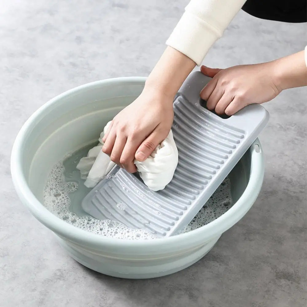 A hand is placing a white fabric washing board into a light blue bowl filled with soapy water.