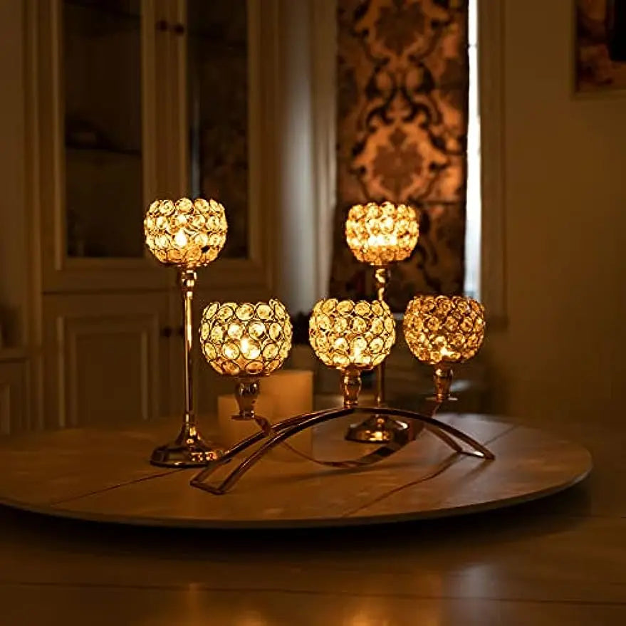 A set of four gold crystal tealight candlesticks displayed on a wooden surface.