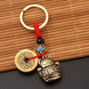 Vintage gold-tone lucky cat keychain with a round coin charm and red tassel on a bamboo mat.
