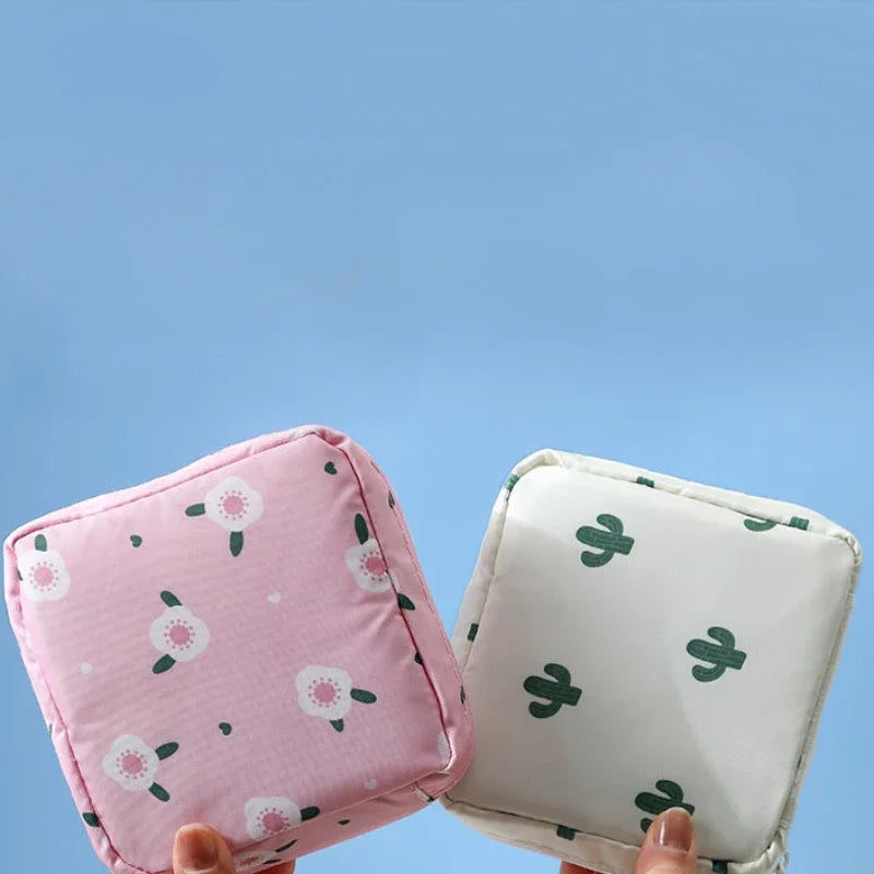 A hand holds a pink floral nylon sanitary pad storage pouch against a light blue background.