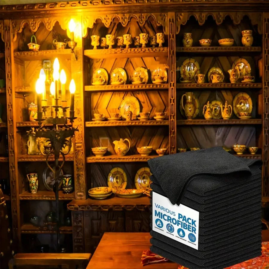 A stack of black reusable microfiber cleaning cloths placed in front of a wooden cabinet display.