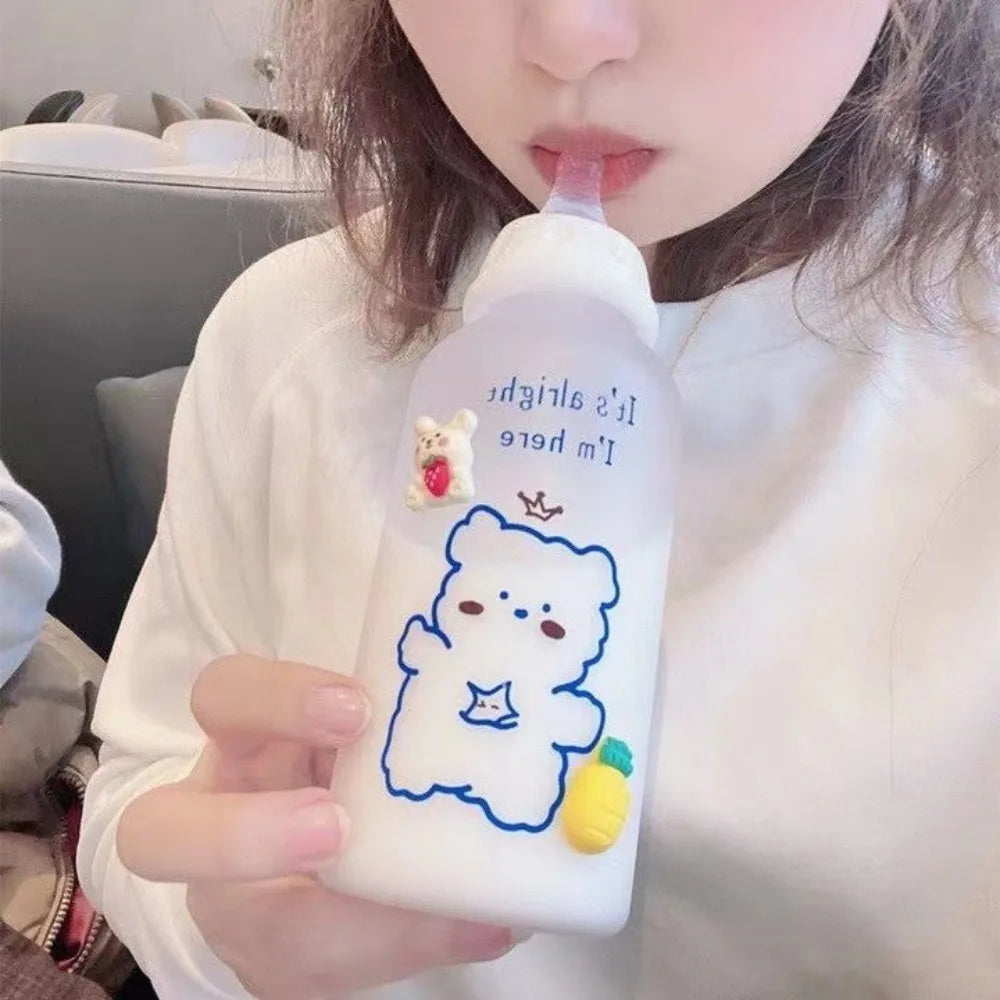 A person holds a white water bottle featuring a blue outline drawing of a bear and a small yellow fruit.