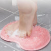 A pink reusable silicone foot scrub brush is shown with wet feet on a tiled surface.
