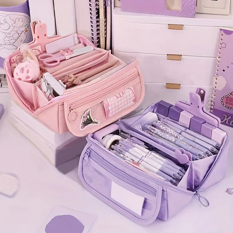 A pink and purple multi-compartment pencil case organizer with various storage slots is shown on a white desk.