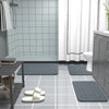 A collection of gray non-slip absorbent bath mats placed on a glossy tiled floor in a bathroom setting.