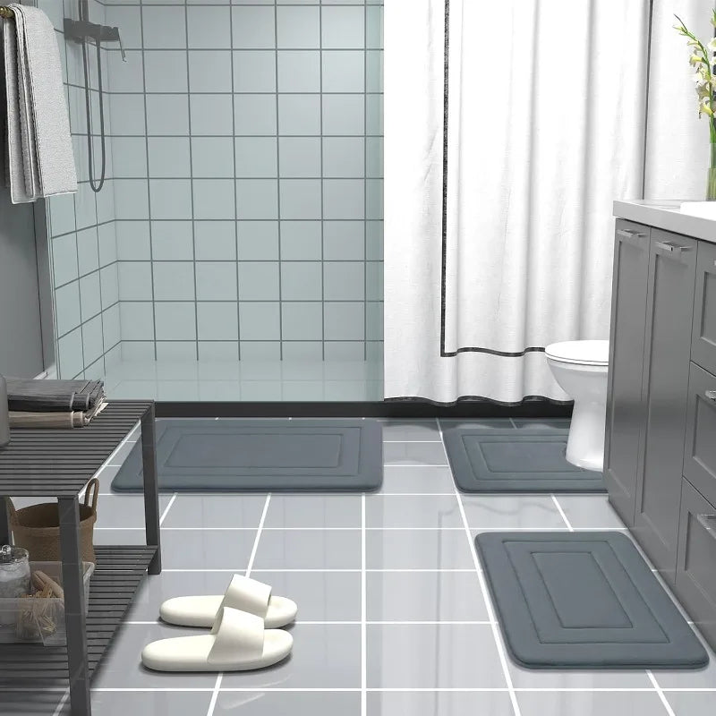 A collection of gray non-slip absorbent bath mats placed on a glossy tiled floor in a bathroom setting.