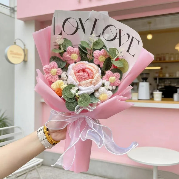 A pink bouquet of artificial roses with a LOVE message is held by a hand against a light pink background.