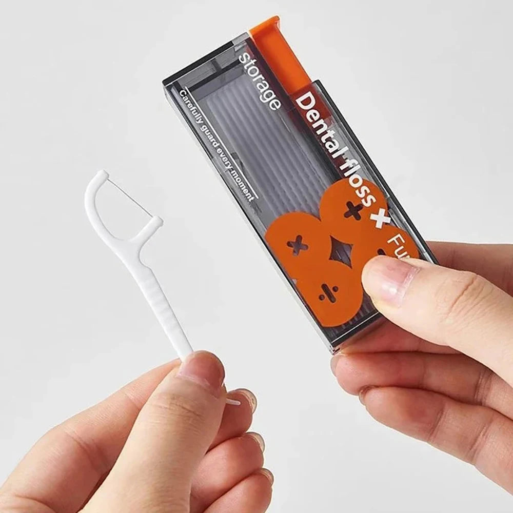 A hand holds a portable automatic floss storage dispenser with orange and black components.
