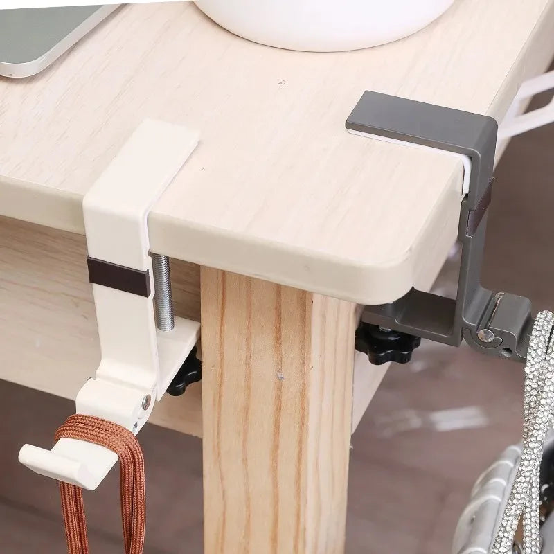 A close-up of an adjustable desk hook bag hanger attached to a light wood desk surface.