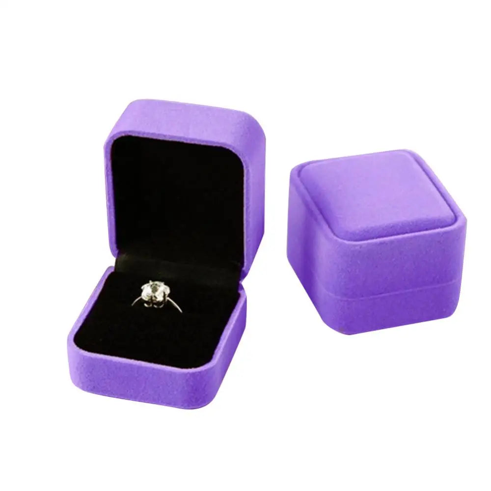 A purple velvet jewelry box with an open lid displaying a silver ring.