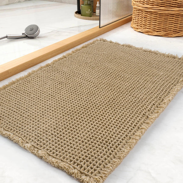 Beige Waffelstruktur Bademat auf weißem Marmor neben Holz- und Rattan-Dekoration.
