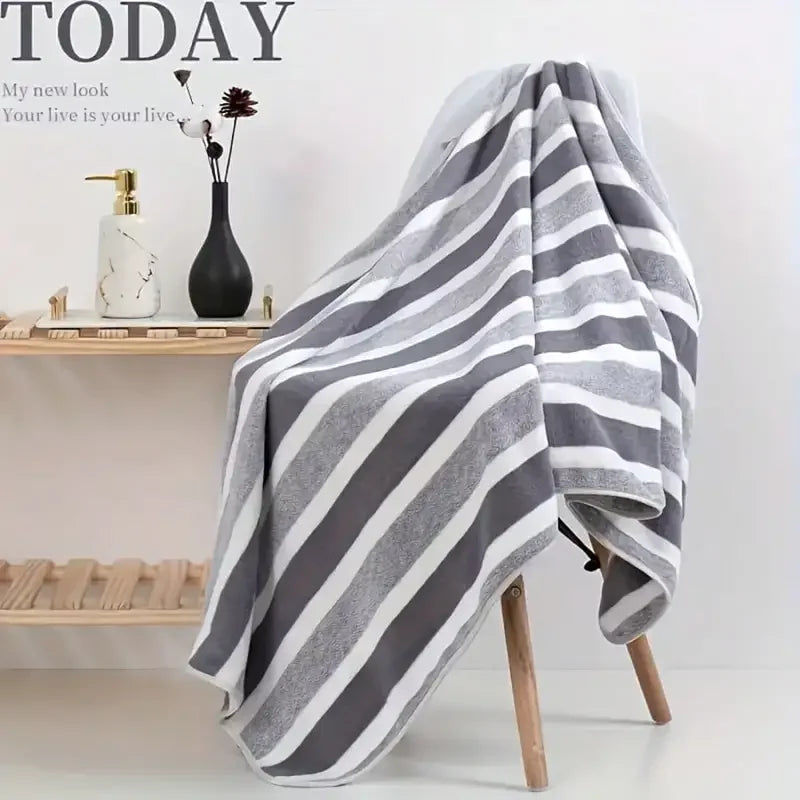 A gray and white striped bath towel draped over a wooden stand next to a vase and on a shelf.