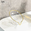Clear oval plastic soap dish with gold rim and drainage holes resting on a white surface.