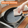 A hand is cleaning a non-stick frying pan with a beige cotton waffle weave towel on a stovetop.