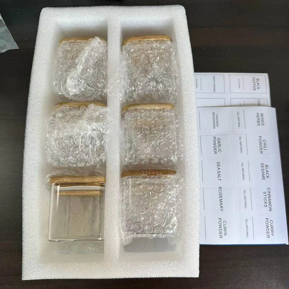 Five glass spice jars with bamboo lids are arranged in a white foam insert.