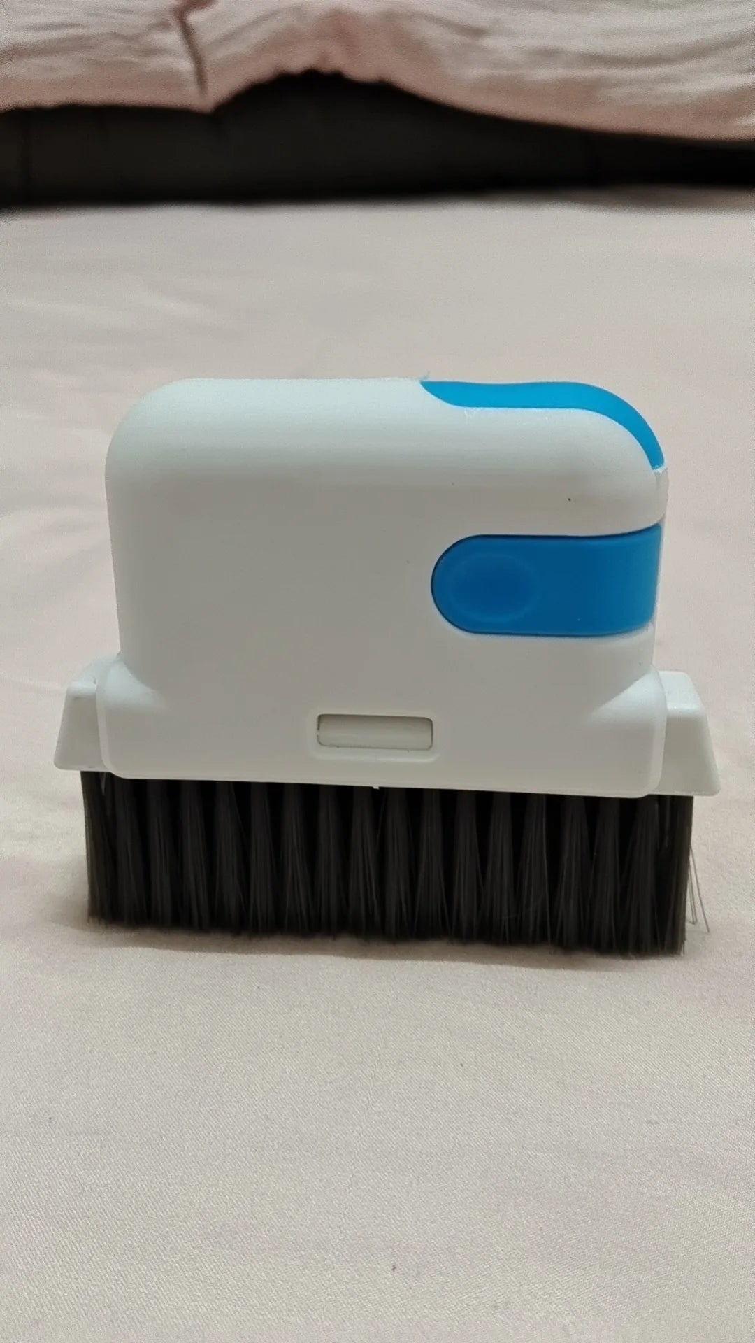 Una brocha de limpieza blanca con mango azul y cerdas negras sobre una superficie clara.
