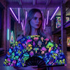 A woman holds a holographic gradient rave hand fan with colorful floral and mushroom patterns in a dimly lit industrial setti