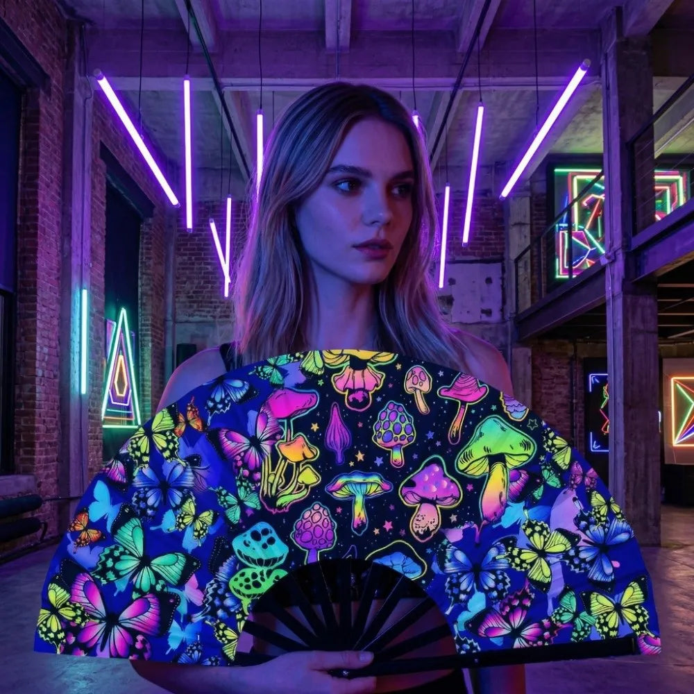 A woman holds a holographic gradient rave hand fan with colorful floral and mushroom patterns in a dimly lit industrial setti