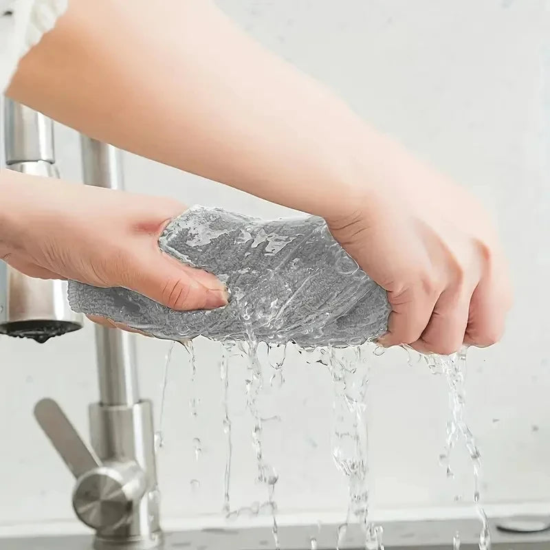 A hand is holding a gray reusable microfiber cleaning cloth under running water.