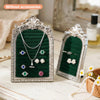 Présentoir de bijoux argenté avec fond velours vert foncé, mettant en valeur diverses colliers et boucles d'oreilles.