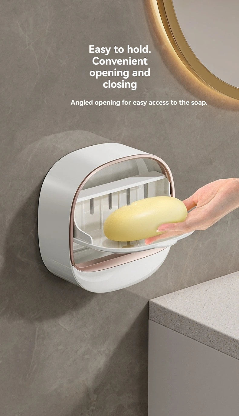 A hand is holding a yellow soap bar inside a white wall-mounted soap dish with an angled opening.