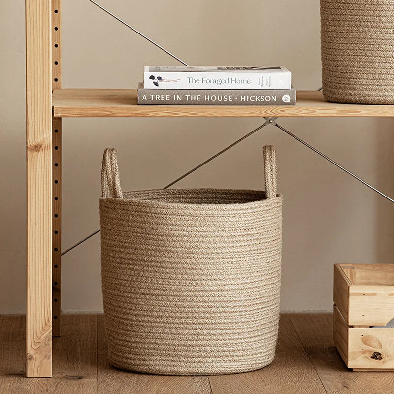 A woven natural cotton rope storage basket sitting on a wooden shelf next to a book.