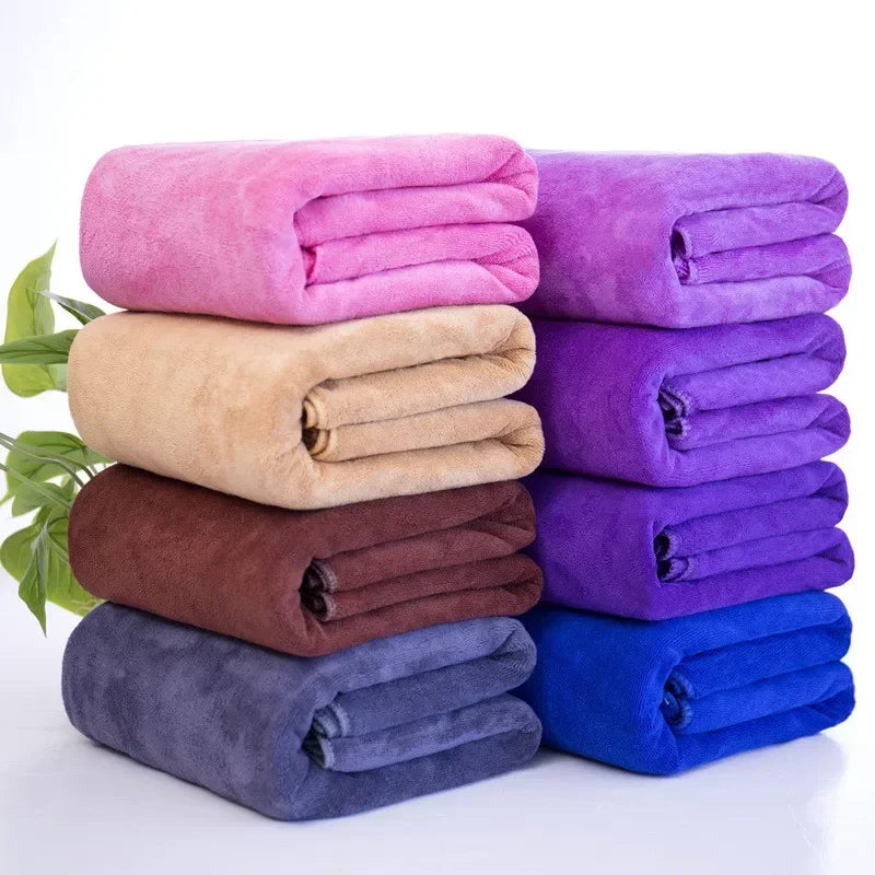 A stack of various colored ultra-absorbent microfiber bath towels in shades of pink, purple, beige, brown, and blue.