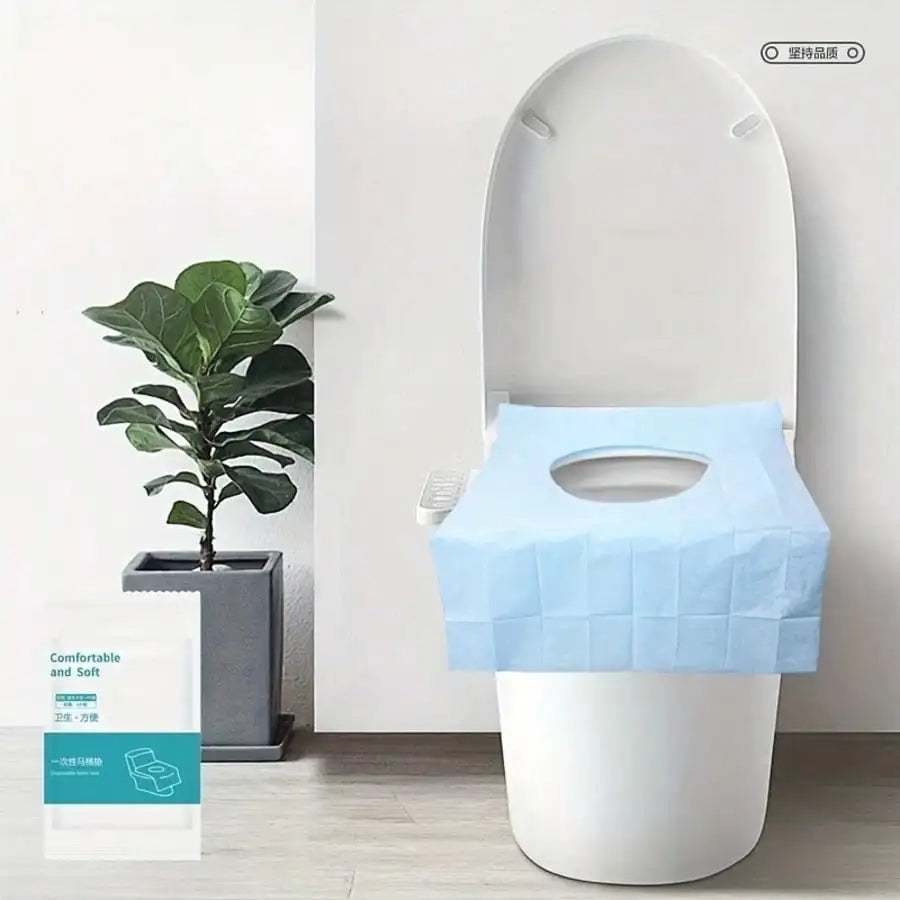 A white toilet with a light blue disposable seat liner placed on top, next to a potted plant.