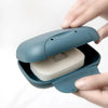 A hand opens a teal portable travel soap box to reveal a white bar of soap inside.